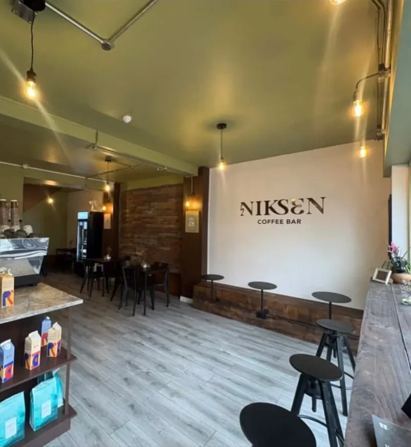Inside Niksen Coffee Bar: filament pendant lights, galvanised conduit along the ceiling and the Niksen sign on the wall