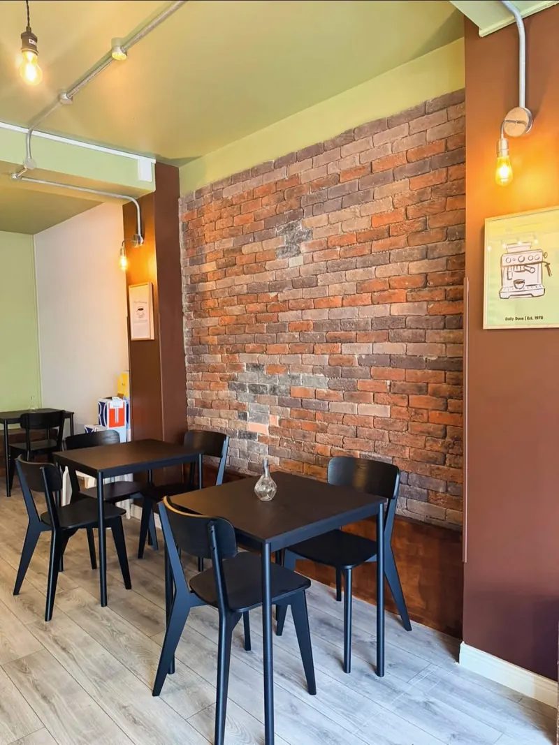 Tables beside an exposed brick wall, lit by wall lights fed through surface conduit