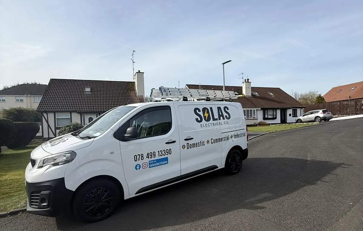 The white Solas Electrical Co. van with ladders on the roof, parked on a residential street under a blue sky